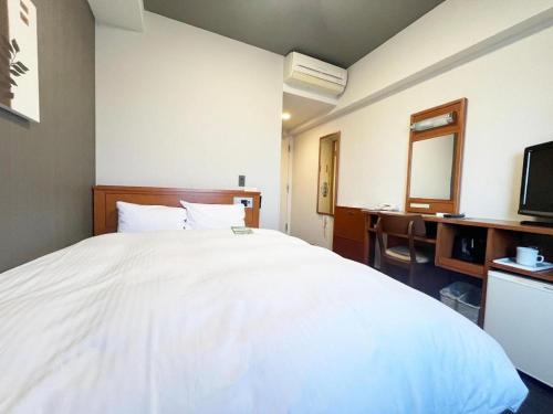 a bedroom with a large white bed and a desk at Hotel Route Inn Furukawa Ekimae in Osaki