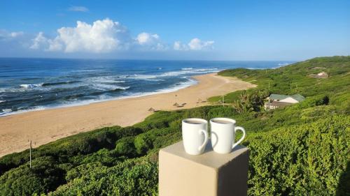 two white coffee mugs sitting on a ledge overlooking a beach at The View - Xai Xai Mozambique Xai Xai Beach Front 180 Degree Sea Views in Xai-Xai