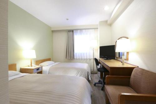 a hotel room with two beds and a desk and a television at Centia Hotel Naito in Kofu