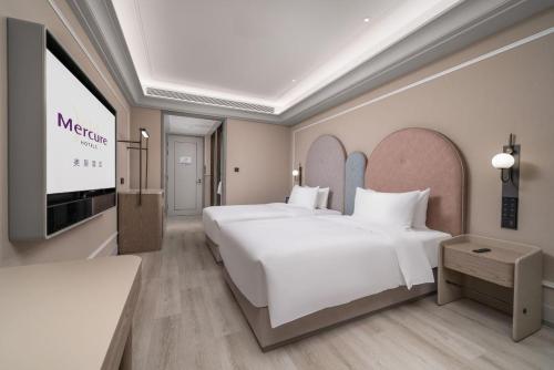 a hotel room with two beds and a flat screen tv at Mercure Guangzhou Financial City in Guangzhou