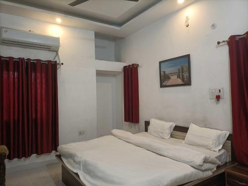 a bedroom with a bed with white sheets and red curtains at Hotel O by OYO Allahabad Property in Bhīta