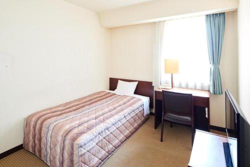 a hotel room with a bed and a desk and a window at Marroad Inn Kumagaya in Kumagaya
