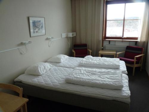 a bedroom with a bed with white sheets and two chairs at Vålådalens Fjällstation in Vålådalen