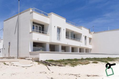 a white building on the beach next to the sand at HOTIDAY Apartment Collection - Torre Lapillo in Porto Cesareo
