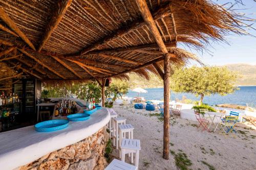 a bar on the beach with chairs and a straw umbrella at Stone Beach Residence - Adults Only Resort in Qeparo