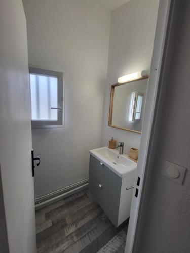 une salle de bain blanche avec un lavabo et un miroir dans l'établissement Maisonnette Mail Rochelongue location samedi au samedi, au Cap d'Agde