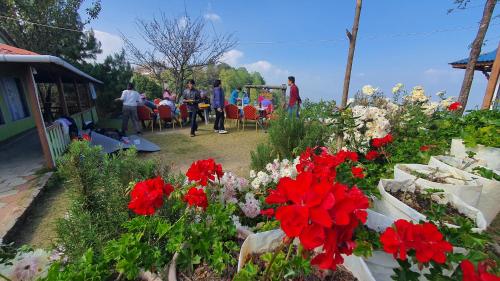 a group of people standing around a garden with red flowers at Mundum Farm Stay in Dhulikhel
