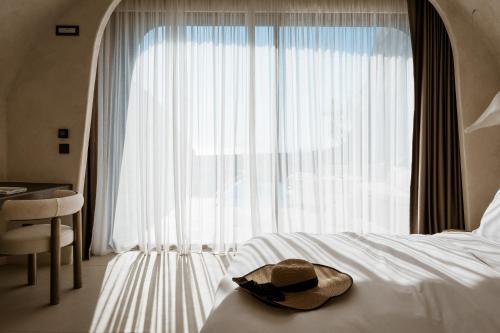 a hat sitting on a bed in front of a window at One of One Hotel in Imerovigli