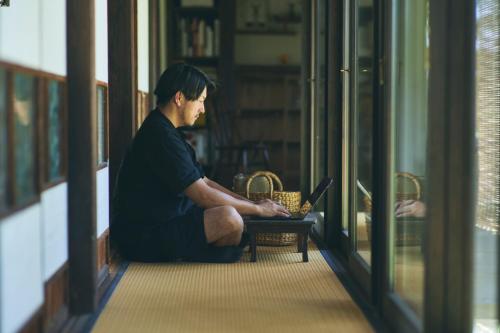 a man sitting on a bench with a laptop at MUJI BASE kamogawa in Kamogawa