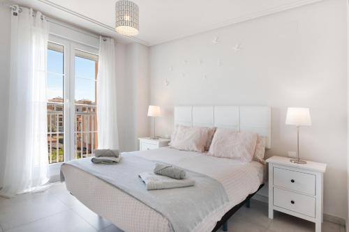 a white bedroom with a large bed and a window at Apartamento en Isla Canela in Ayamonte