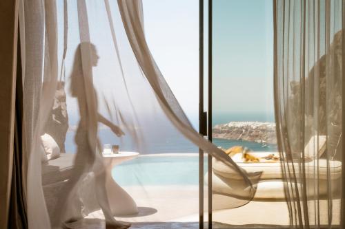 a woman standing in a window looking out at the ocean at One of One Hotel in Imerovigli