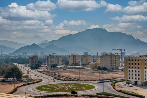 a city with buildings and a road with mountains in the background at Japandi Mountain Escape in Khor Fakkan
