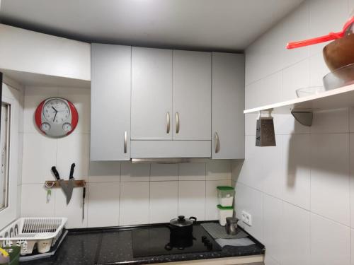 a kitchen with white cabinets and a clock on the wall at Hab Moderna A 20 Minutos del Centro de Barcelona in Santa Coloma de Gramanet