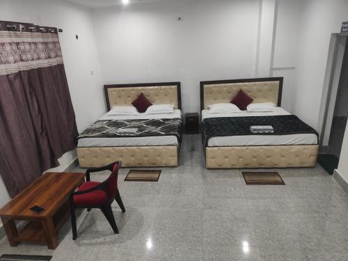 two beds in a room with a table and a chair at Mahadev Hotel And Restaurant in Rudraprayāg