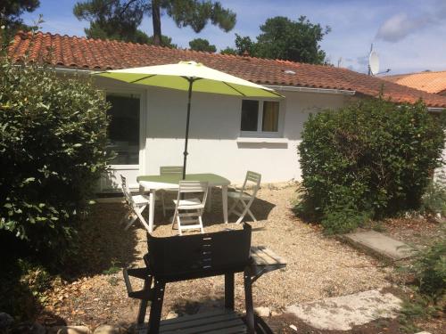 - une table et des chaises avec un parasol en face d'une maison dans l'établissement Studio Bermichan, à Montalivet-les-Bains