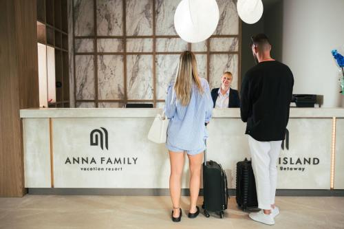 a man and a woman standing at a counter with luggage at Anna Island in Pefkohori