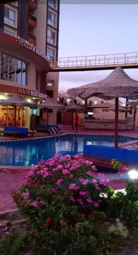 einen Pool mit rosa Blumen und einem Sonnenschirm in der Unterkunft مستقبل للشقق الفندقيه والالعاب المائيه in El-Alamein