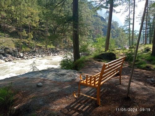 a wooden bench sitting in front of a river at Crown Bliss - Riverside Luxury Paradise in Kasol