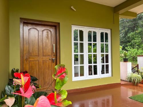 a front door of a house with red flowers at Srishti Homestay in Madikeri