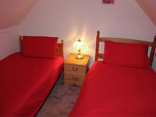 two beds in a room with red sheets and a lamp at 3 Bed in Isle of Barra CA295 in Ersary