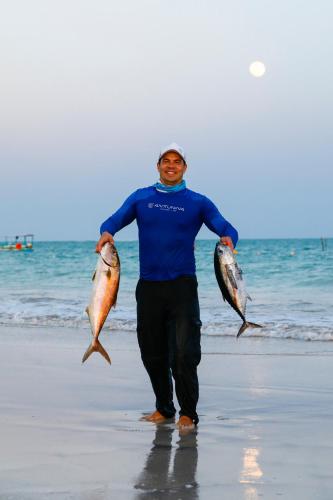 a man walking on the beach holding two fish at Anttunina Pousada e SPA in Maragogi