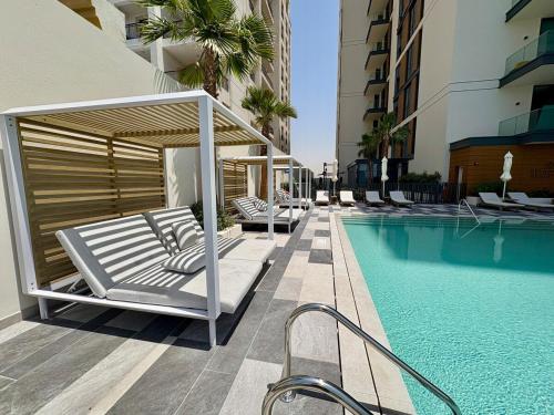 a swimming pool with chairs and a bed next to a building at Stylish Studio in JVC with Pool, Gym, Balcony & Modern Comforts in Dubai