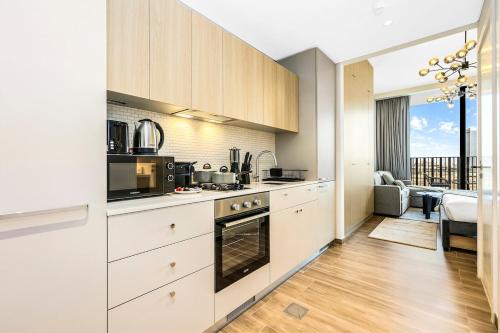 a kitchen with white cabinets and a living room at Stylish Studio in JVC with Pool, Gym, Balcony & Modern Comforts in Dubai