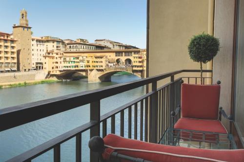 a red chair sitting on a balcony overlooking a river at Hotel Lungarno - Lungarno Collection in Florence