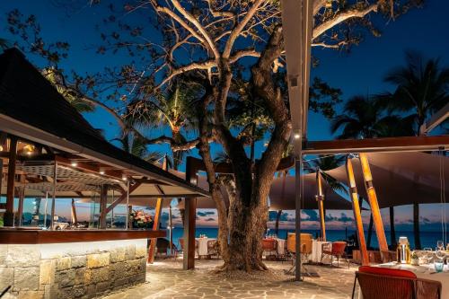 a tree in front of a restaurant with the ocean at Royal Palm Beachcomber Luxury in Grand Baie