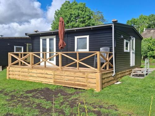 Una pequeña casa negra con una terraza de madera y una sombrilla. en Rural holiday home, en Boornbergum