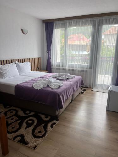 a bedroom with a bed with purple sheets and windows at Guest House Raffe in Dobrinishte