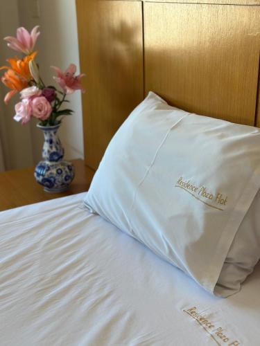 a pillow sitting on a bed with a vase of flowers at Plaza Flat in Ribeirão Preto