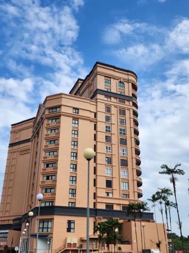 a tall tan building with palm trees in front of it at Riverbank Suites Kuching Waterfront in Kuching