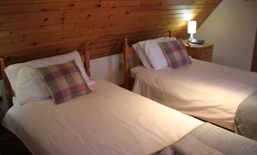 two beds in a room with wooden walls at Heather Cottage in Lairg