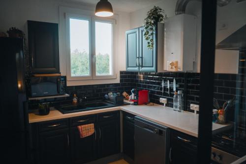 d'une cuisine avec des placards noirs, un évier et une fenêtre. dans l'établissement Cozy & bright apartment, à La Celle-sous-Gouzon
