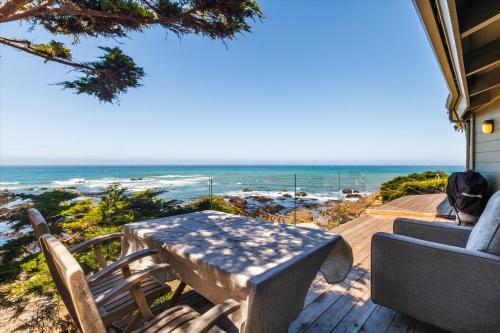 eine Holzterrasse mit einem Tisch, Stühlen und Meerblick in der Unterkunft Sunset Sanctuary Oceanfront Luxury Monthly Newly remodeled in Cambria