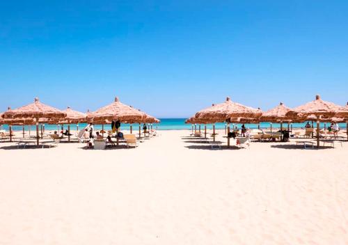 a beach with umbrellas and people sitting on the sand at La Chiocciola Apartments in Rosolini