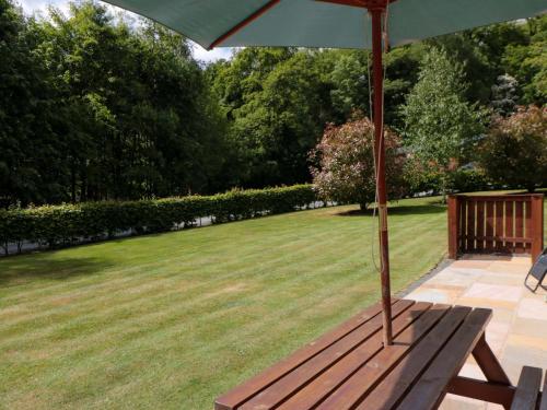 a wooden bench with an umbrella on a lawn at Ryedale Country Lodges - Willow Lodge in York