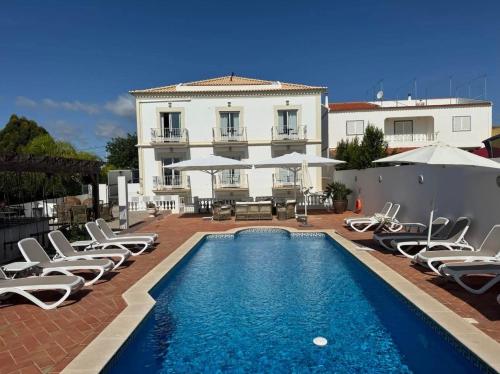 a pool with chairs and umbrellas in front of a building at Quinta do Pedro in Luz de Tavira