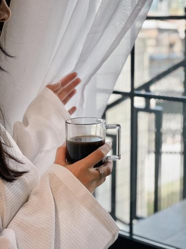 a woman holding a glass of coffee in front of a window at Tiroents Hotel in Gyumri