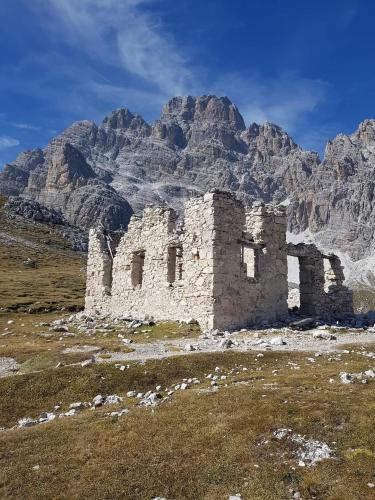 an old building on a field with mountains in the background at Appartamento Comelico Dolomiti in Candide