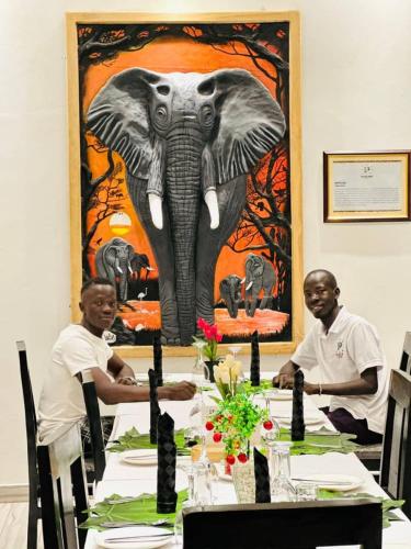 two men sitting at a table with an elephant painting at Kacoke Madit Hotel and Cultural Centre, Gulu in Gulu