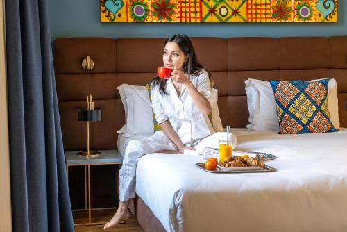 a woman sitting on a bed drinking a cup of coffee at Hotel Rovereto in Rovereto