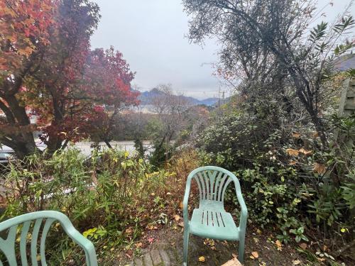 two green chairs sitting in a garden with trees at Retro cosy unit with lake views and patio walk to town in Queenstown