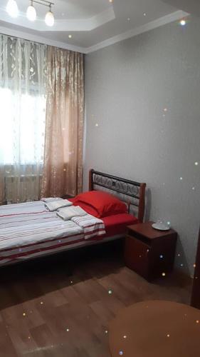 Un dormitorio con una cama con almohadas rojas y una ventana. en Гостевой Дом, en Karagandá