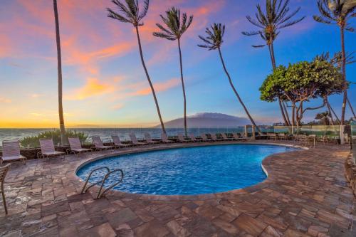 a swimming pool with chairs and palm trees at Watch Whales and Sunsets from your Bed - Double Master Sunset Suite in Kihei