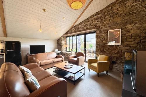 Elle comprend un salon doté d'un mobilier en cuir et d'un mur en pierre. dans l'établissement Spacieuse maison bretonne Plage à 3 mi, à Sarzeau
