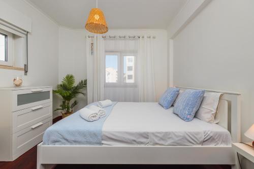 a white bedroom with a large bed with blue pillows at Breeze Beach House in Setúbal