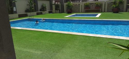a swimming pool with green grass and a person in it at Bel Appartement à Résidence Tej Bhar 2 Mrezga Hammamet in Hammamet Nord