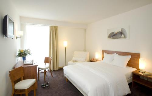 アントエギュ・シュル・トリュイエールにあるHôtel La Rivièreの白いベッドとデスクが備わるホテルルームです。